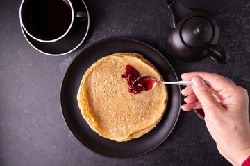 Oatmeal pancakes with lingonberry jam on a black plate on a black background.