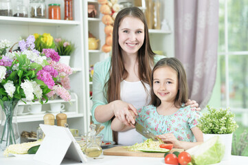 smiling pregnant mother and daughter cooking together at kitchen