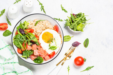 Savory breakfast. Oatmeal porrige with salted salmon, egg and fresh salad. Top view on white table with copy space.