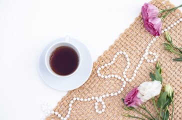 Obraz na płótnie Canvas Beautiful composition for blog post in Instagram. Cup of tea or coffee, flowers and beads on white table with brown napkin. Free moment to relax and enjoy the wonderful. Close-up