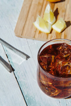 cola in a glass with ice and lemon on a white wooden base