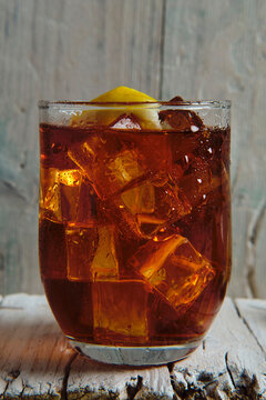 close-up of a glass full of cola with ice and lemon on a wooden base