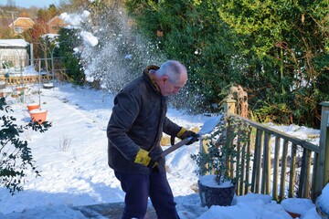 Senior man clearing snow off his decking .