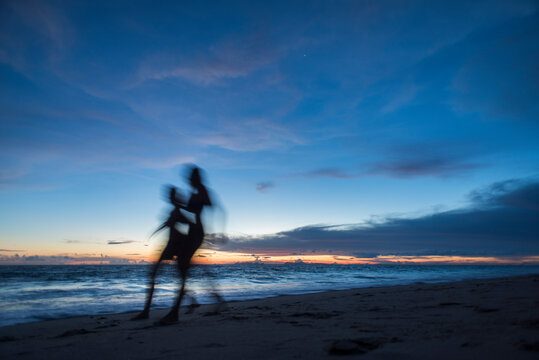 Two women running on a white sand beach at sunset time, Koh Lanta Island, Thailand.