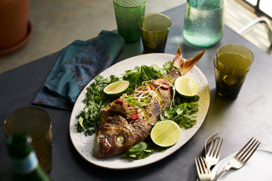 Roasted whole fish dish in a table setting with glasses and napkin