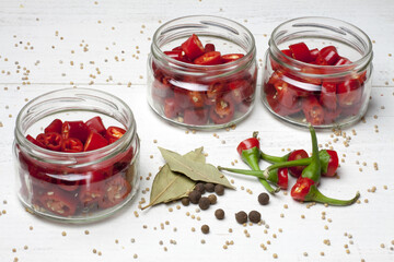 Chillies, cut and placed in jars, waiting to be marinated. On a white table with tails of peppers and spices used for pickling.