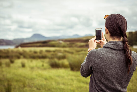 Young woman photographing Scottish Highlands mountain landscape