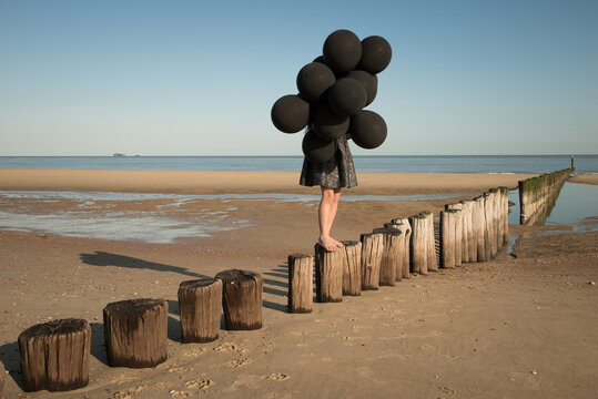 Girl in black dress holding bunch of black balloons on the beach