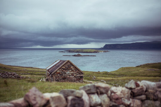 Stone hut sits on remote coastline with cliffs and clouds