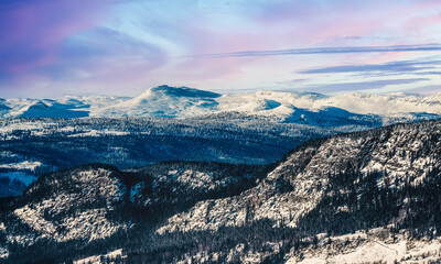View over a majestic mountain wilderness landscape in winter with dramatic sunset clouds.