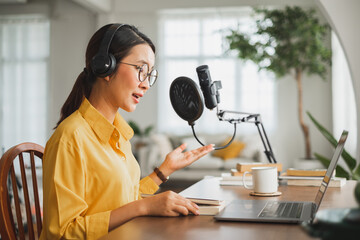 Asian woman recording a podcast on laptop computer with microphone while online live streaming at...