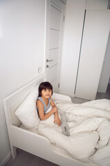 Obraz premium child boy lies in a white children's bed with a blanket in a room with toys rabbits