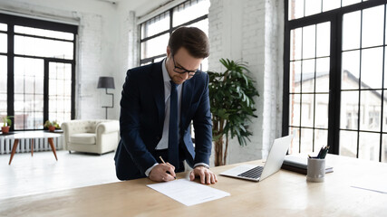 Young Caucasian businessman in suit sign business paperwork on desk in modern office, close deal...