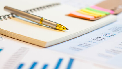 Golden pen on the background of a notebook and financial graphics