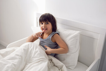 child boy lies in a white children's bed with a blanket in a room with toys rabbits