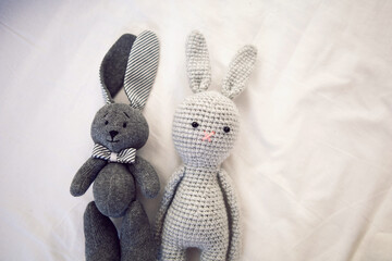 two knitted rabbit toys lie under a blanket in a white bed
