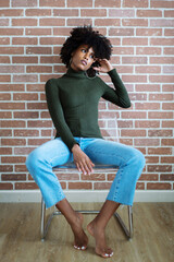 Beautiful black woman with afro hair sitting on the chair against the brick wall background