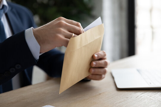 Crop close up of male employee or CEO sit at table open envelope with postal letter or mail. Caucasian businessman consider receive post paper correspondence or document message at workplace.
