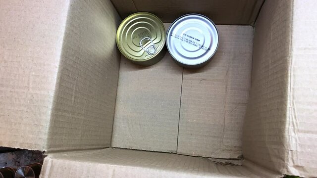 Collect food and groceries in a box for donations and help to the elderly - A man collects a box of humanitarian aid for the needy: rice, cereals, canned goods in tins.