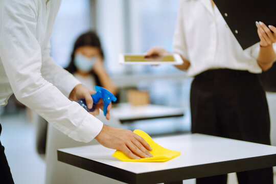 Cleaning and disinfection of the desktop. Man in protective sterile mask cleans the working desk with the wiping cloth and antibacterial sprayer. Covid-2019.