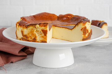 San Sebastian cheesecake on top on a white plate on a gray concrete background. Traditional Spanish dessert. Copy space