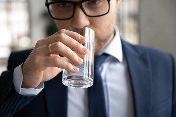 Crop close up of Caucasian businessman hold glass drink clean clear mineral still water feeling thirsty. Dehydrated male employee or worker enjoy aqua for body refreshment. Healthy lifestyle concept.