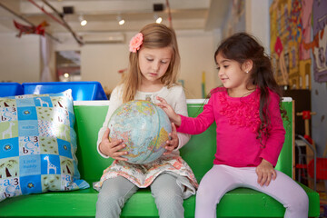 Girls looking at globe while sitting on green seat at child care