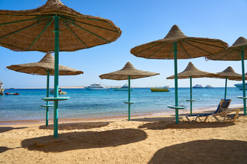 Beach with clean white sand on a sunny day. Umbrellas and sun lounger on the seashore against the blue sky