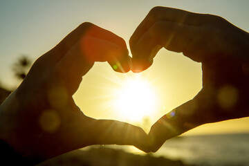 Heart shape with childs hands over sunset sky background