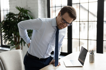 Unhappy unwell male employee suffer sitting in incorrect posture at desk in office, have backache...