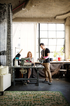 Fashion designers discussing while working against windows at workshop
