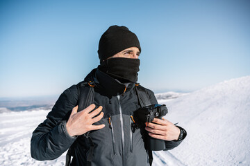 Portrait of an attractive photographer in the snow with professional camera in his backpack while walking.