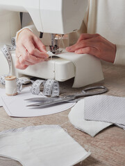 Sewing process, close up seamstress hands sew white clothes with sewing machine.