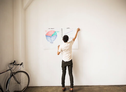 Full length of businessman sticking graphs on white wall at creative office