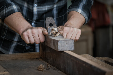 A male carpenter is using a planer to scrape the wooden surface.