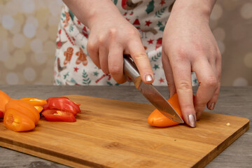 A woman in a kitchen cutting up orange and red peppers on a wooden chopping board home cooking concept