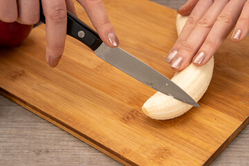 A woman in a kitchen cutting up a banana on a chopping board, fruit salad healthy eating concept