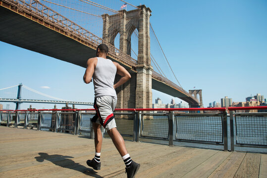 Rear view of man running on boardwalk against Brooklyn Bridge