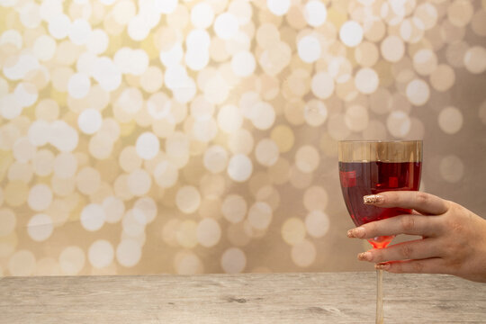 A Woman's Hand With Long Elegant Nails Holding A Glass Of Rose Wine On A Glittery Gold Background