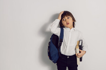 child boy with a book textbook and backpack stands on a white background