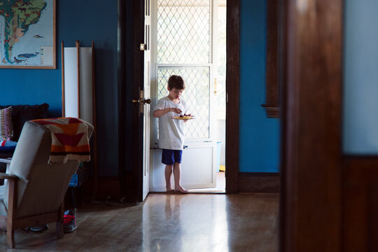 Boy eating food while standing at doorway