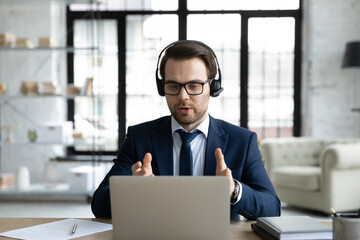 Successful young Caucasian businessman in earphones look at laptop screen consult business client...