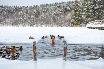 Beautiful boy bathing and swimming in the cold water of a lake or river among the ducks, cold therapy, ice swim with forest trees on background