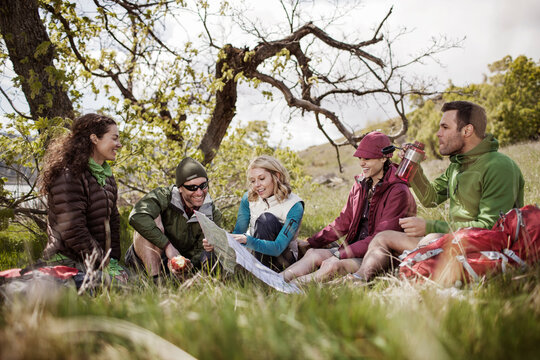 Happy hikers looking at map while sitting on grassy field
