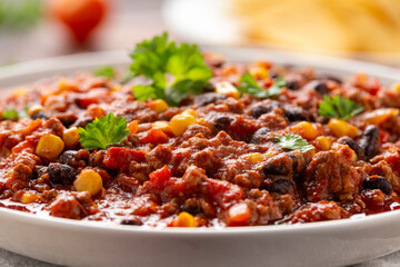 Chilli con Carne with tortilla chips and cheese in white bowl. Mexican food.