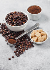 Fresh raw organic coffee beans in white bowl and powder on ligh background with cane sugar and round steel scoop.