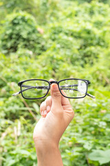 hand-held glossy black square glasses against a backdrop of rolling hills and greenery © Albert