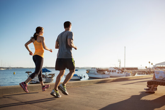 Rear view of male and female athletes jogging on pier by harbor