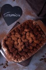 Tiramisu cake sprinkled with cocoa powder. Italian dessert. The name of the dessert is written on the heart-shaped chalkboard. Top view