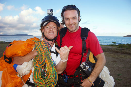 Portrait of smiling friends with parachute standing on field against sea
